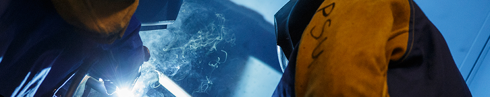 A student practices welding under a professor's supervision