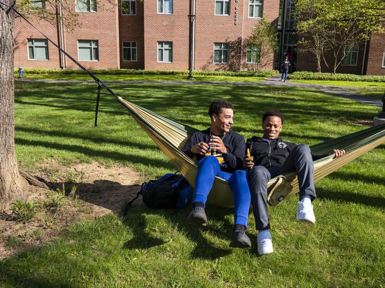 Two students sit on a hammock near residence halls.