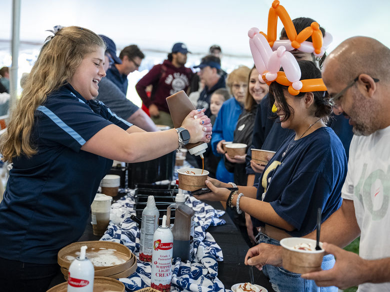 Alumnus wearing balloon animal hat gets Berkey Creamery ice cream from another alumnus