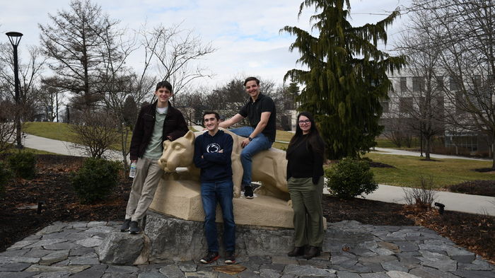Four male students pose for picture on Nittany Lion statue