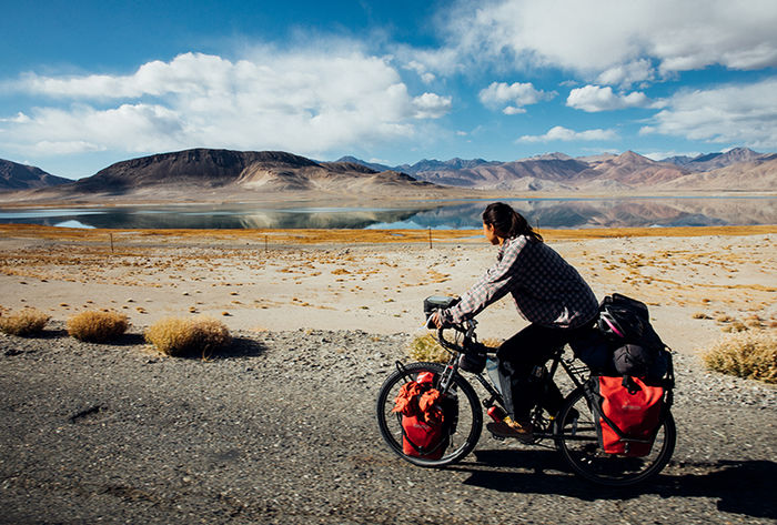 Nicole bikes past a lake on a flat plain, with mountains in the background