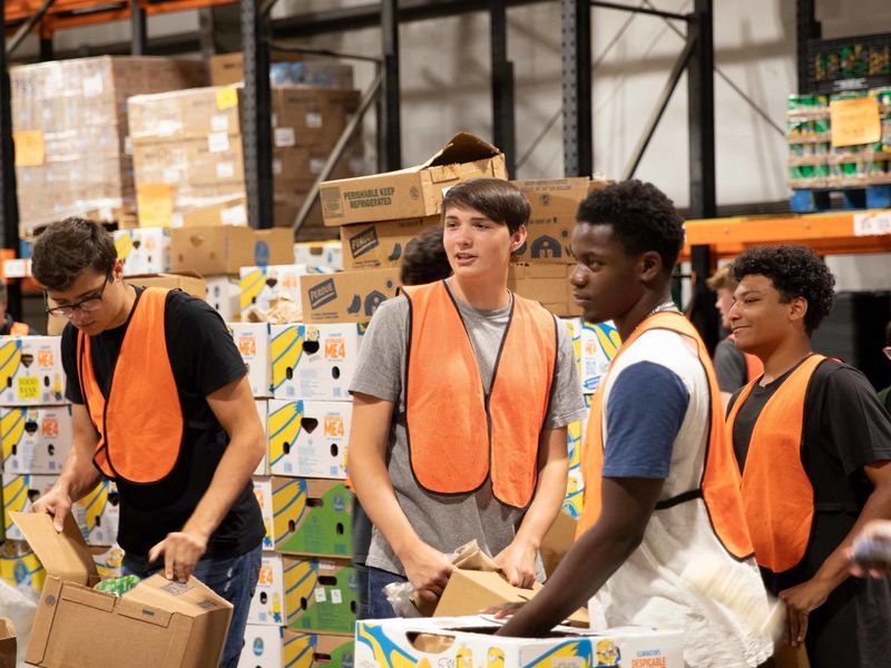Students wearing orange safety vests sort groceries into large cardboard bins