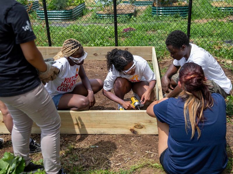 Students wearing protective gear use power tools to build a box made of lumber
