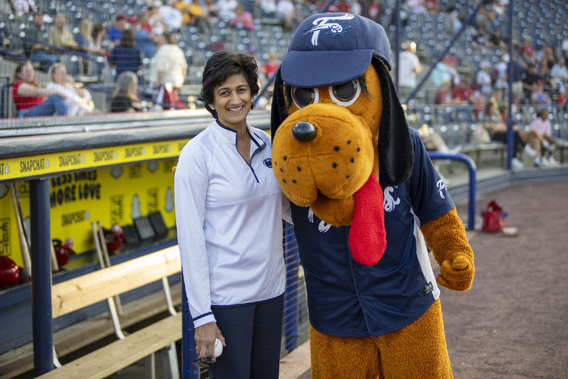 Chancellor Pyati holds a baseball while posing with a hound dog baseball mascot
