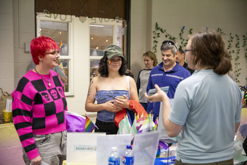 Two students and a faculty member stand at a table with pride flags.