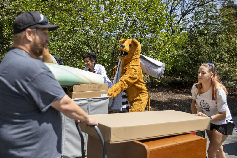 A parent, student, Chancellor Pyati and the Nittany Lion mascot move items into the residence halls