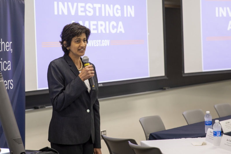 Chancellor Pyati holds microphone in front of signage reading "Investing in America"