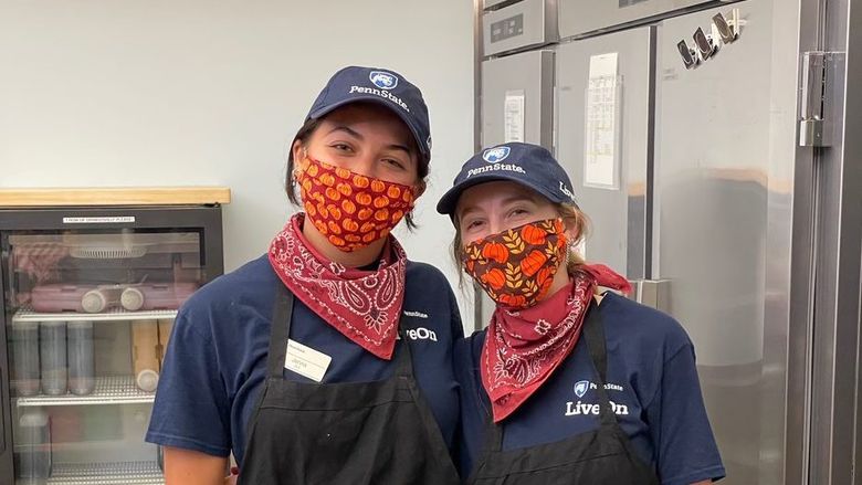 Two women, wearing masks and hats, pose for a photo at work.