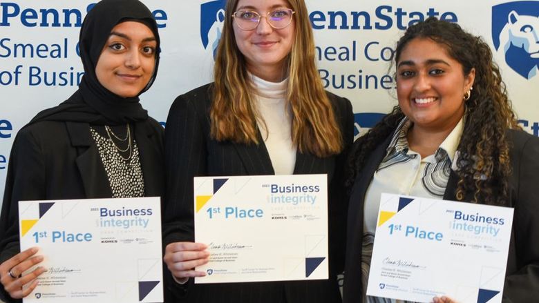 Three female students pose in front of a Penn State Smeal College of Business backdrop holding 1st place certificates