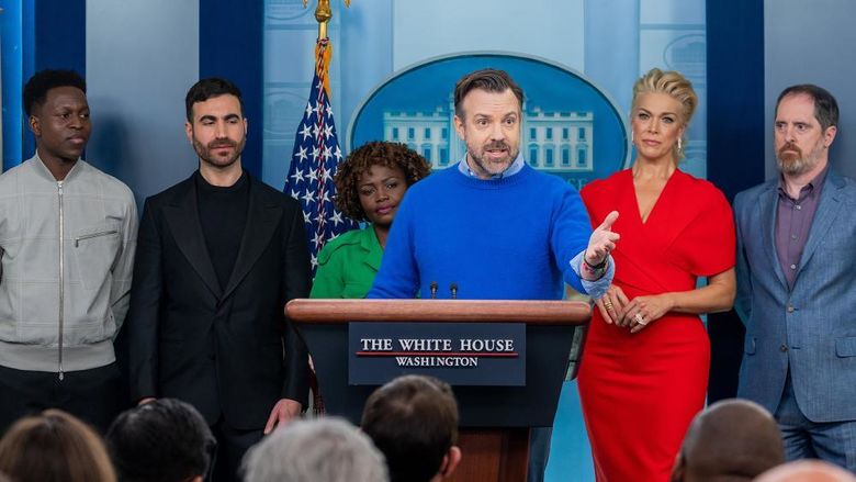Six people stand behind a podium bearing a sign that reads "The White House"
