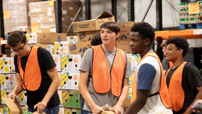 Students wearing orange safety vests sort groceries into large cardboard bins