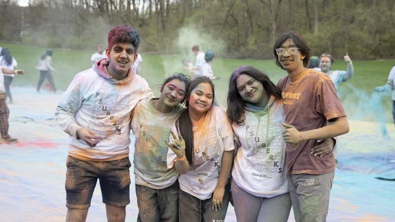 Five students covered in colorful dust smile for the camera.