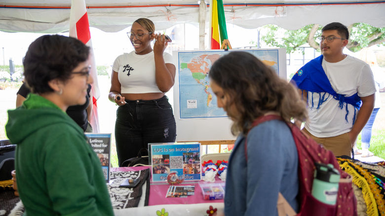 Two students learn about Latinos United for Change club while two students man the table