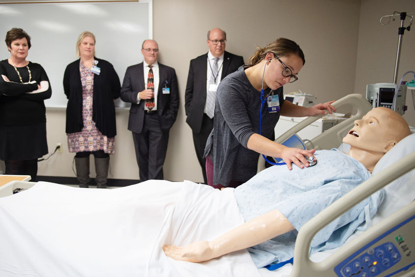 A nurse leans over a mannequin to demonstrate a medical technique