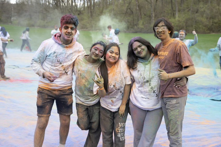 Five students covered in colorful dust smile for the camera.