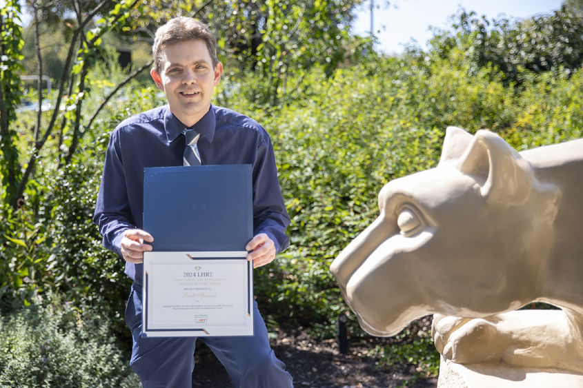 Brett Spencer holding award next to Nittany Lion statue